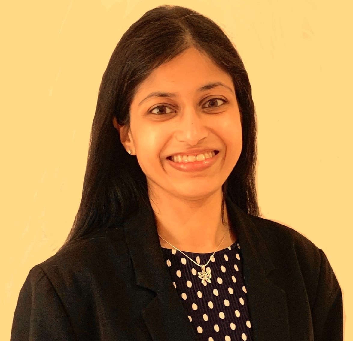 Vidya is a young Asian woman with long black hair smiling wearing a blue dress and black blazer