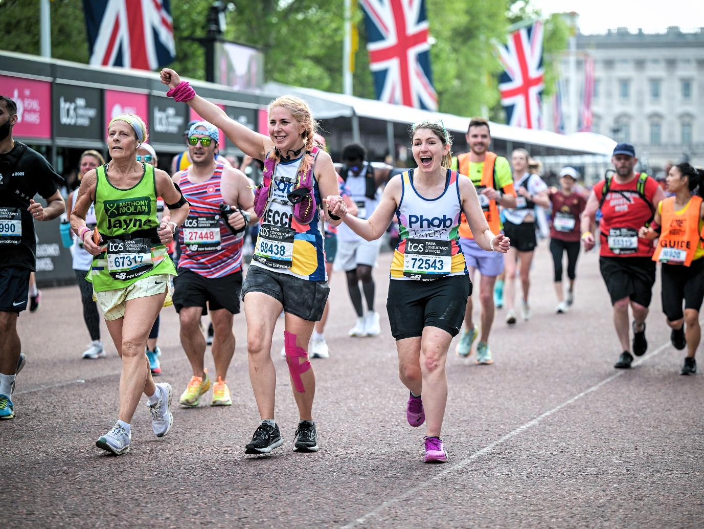 Two people wearing white vests reading "Phab" are holding hands and cheering mid run. You can see other people running behind them and Union Jack flags.