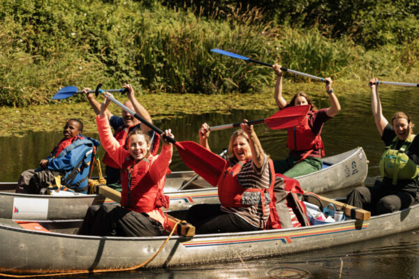 happy adults and children in canoes, holding their oars aloft